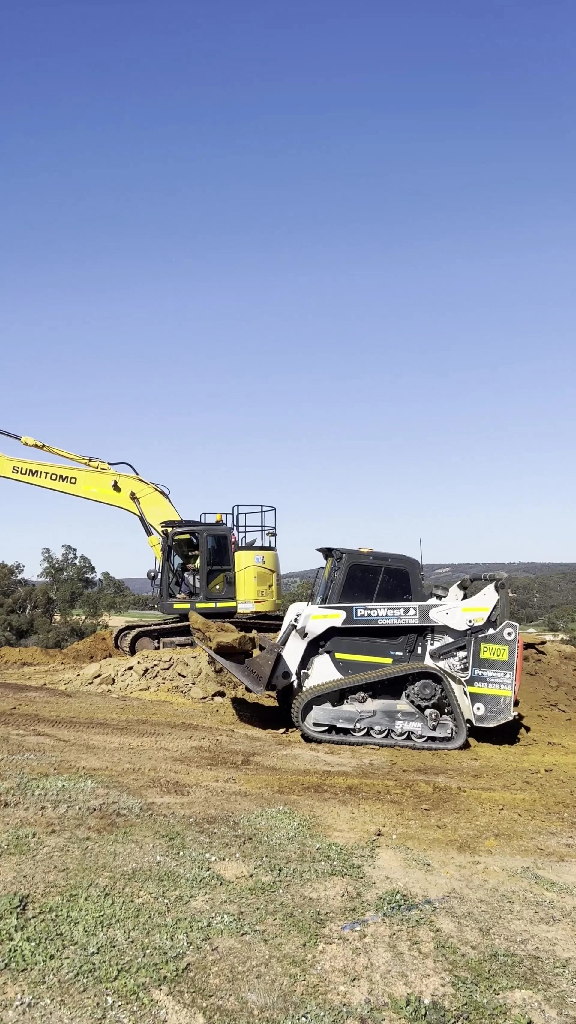 Excavator and posi-track levelling a building pad on a cleared site