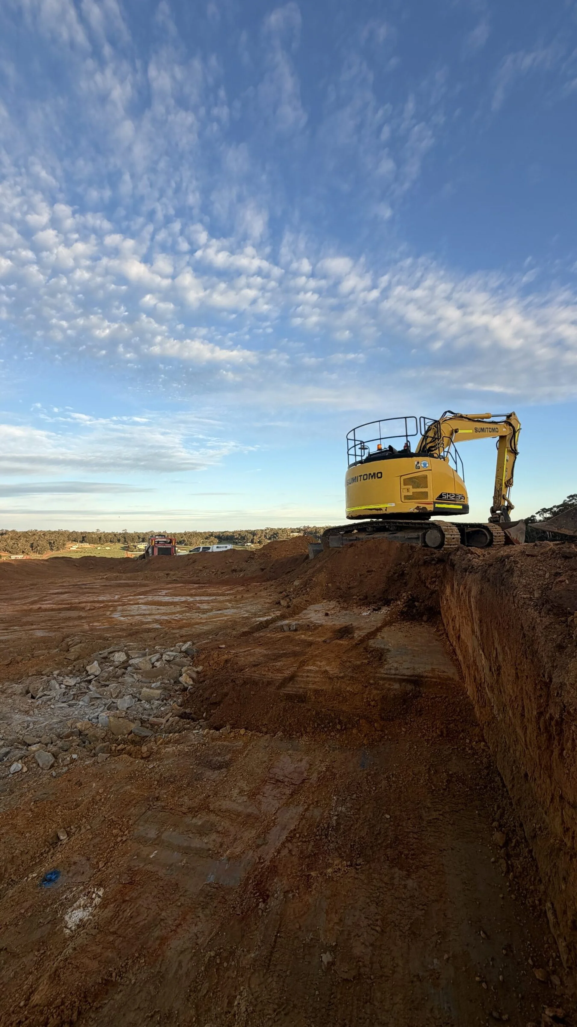 Excavator working along a red laterite cut ridge under an open sky