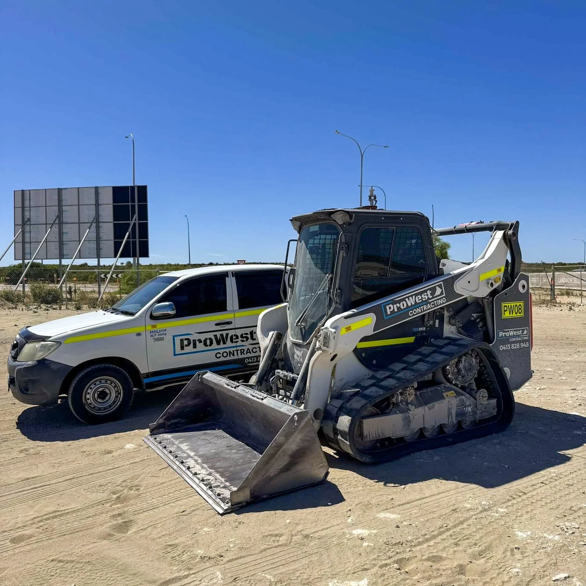 ProWest posi-track PW08 and Hilux ute parked on a sandy roadside site under a clear sky