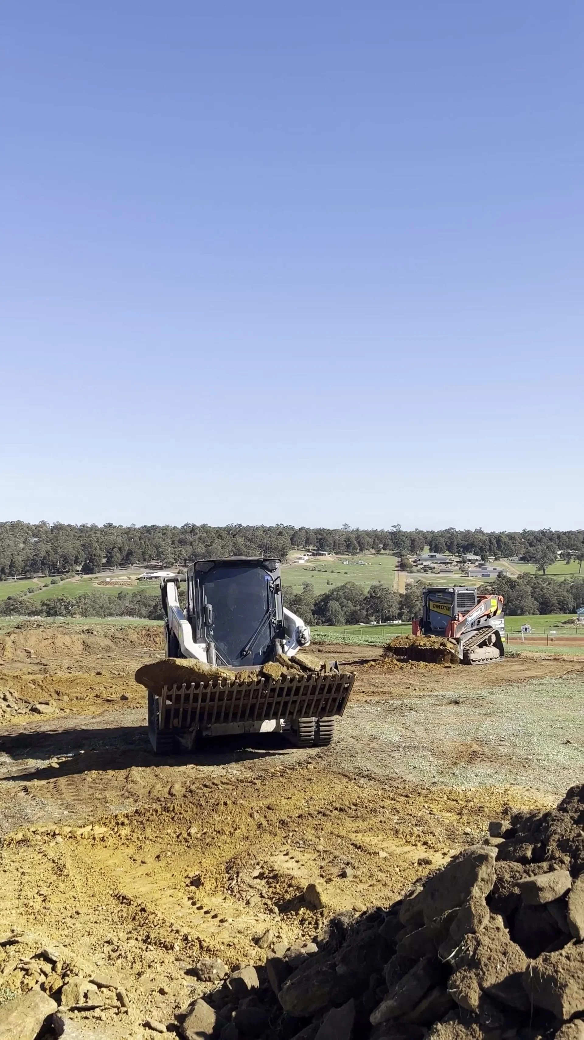 Posi-track carrying a bucket of topsoil across a levelled paddock