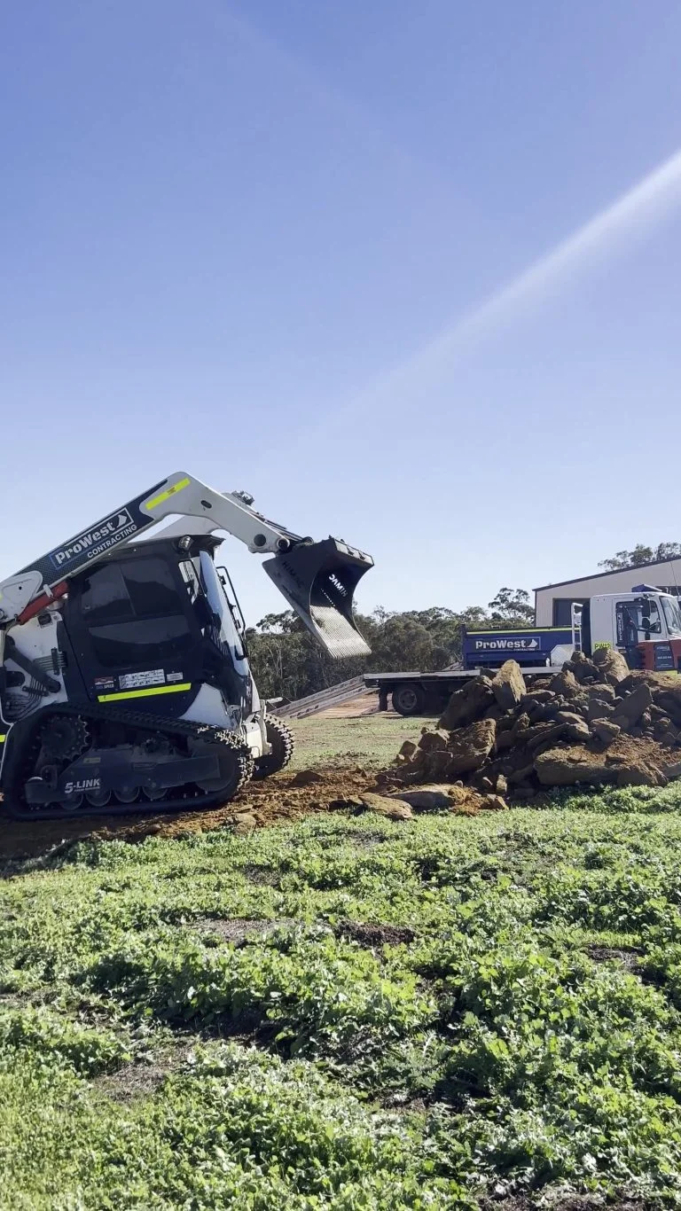Posi-track fitted with a rock grapple clearing rock and debris from a grassed block