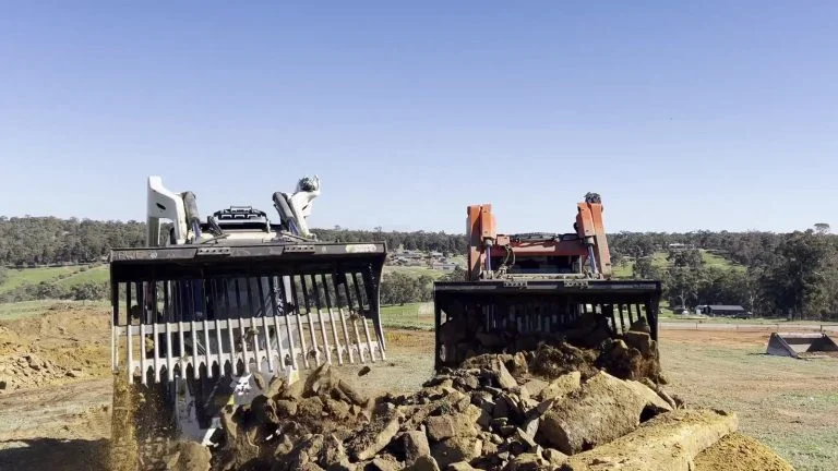 Rock grapple and stick rake buckets side by side with raked rock between them