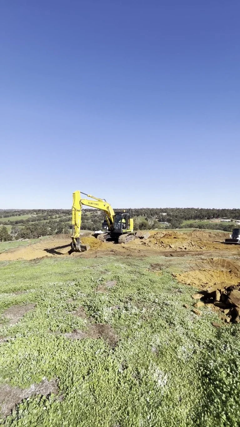 Wide view of site clearing across a grassed block with plant working